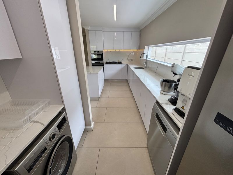 Modern, sleek kitchen featuring high-gloss cabinetry, stone countertops, integrated appliances, and a long horizontal window providing natural light.