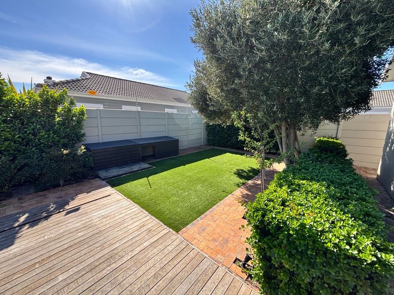 A well-maintained private garden featuring timber decking, brick pathways, artificial lawn, and secure boundary walling with established greenery.