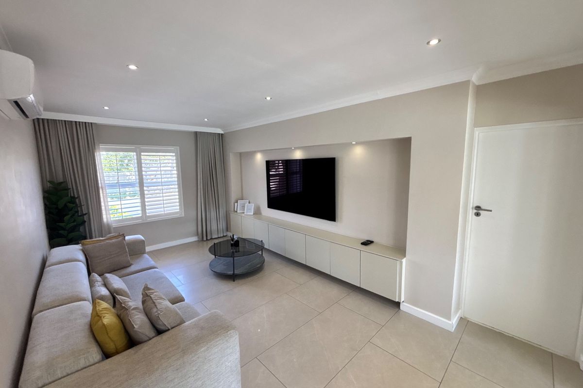Modern living room featuring large format floor tiles, recessed downlights, plantation shutters, and custom built-in cabinetry with integrated television space.