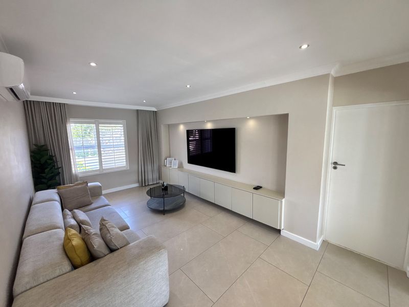 Modern living room featuring large format floor tiles, recessed downlights, plantation shutters, and custom built-in cabinetry with integrated television space.