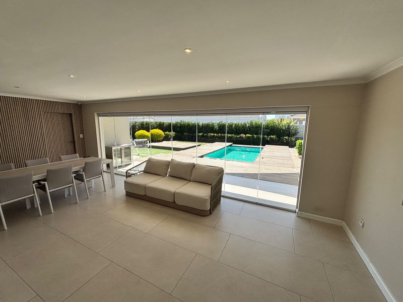 Spacious open-plan living and dining area featuring large format floor tiles, timber slat wall detailing, and seamless stacking glass doors opening to a pool deck.