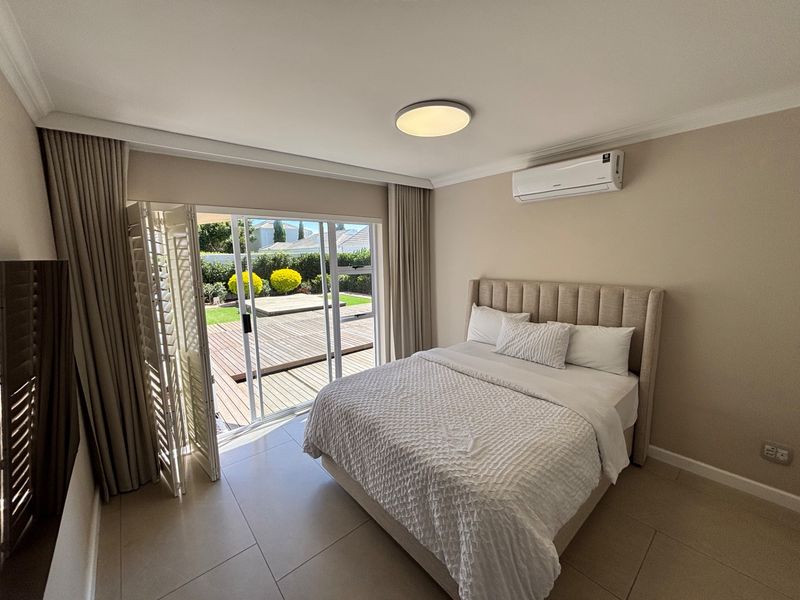 A well-maintained bedroom featuring tiled flooring, a wall-mounted air conditioning unit, and large sliding glass doors providing direct access to an outdoor deck.