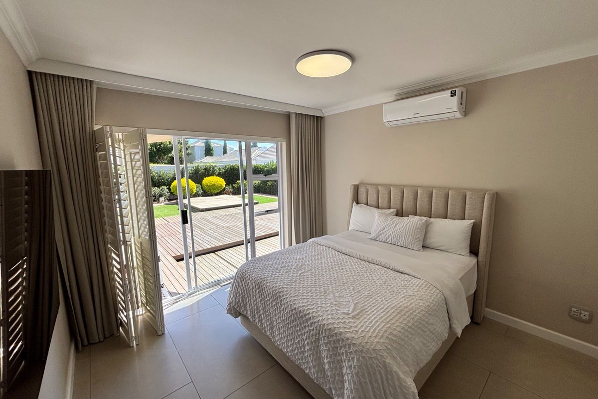 A well-maintained bedroom featuring tiled flooring, a wall-mounted air conditioning unit, and large sliding glass doors providing direct access to an outdoor deck.