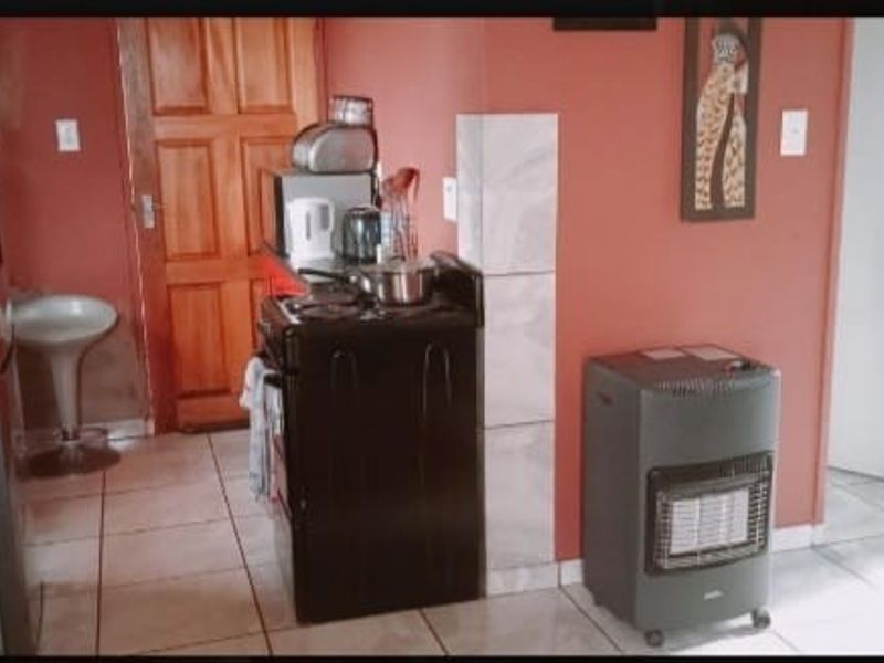 A compact kitchen area featuring tiled flooring, a freestanding stove, and a wooden door, currently finished in a dated color scheme.