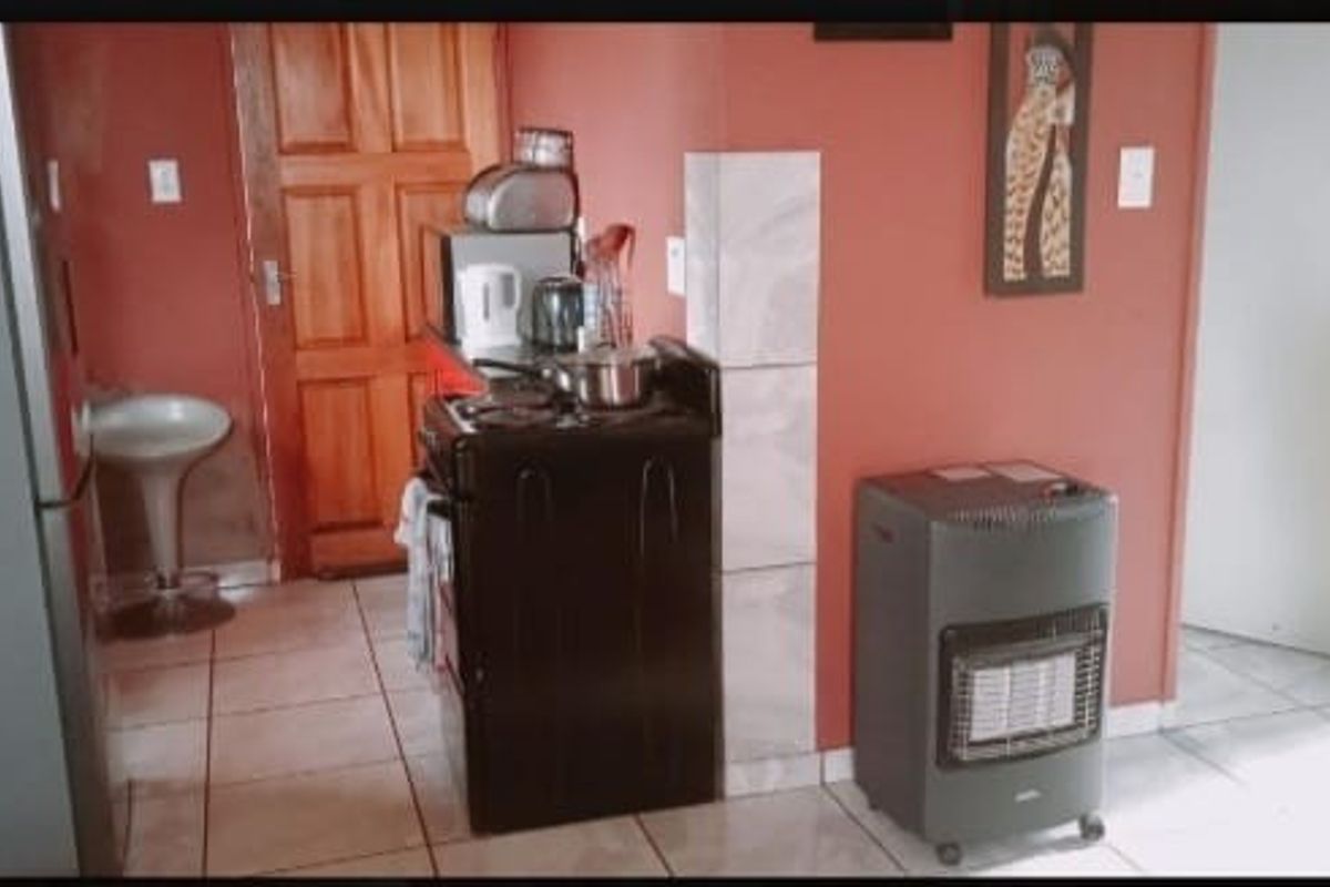 A compact kitchen area featuring tiled flooring, a freestanding stove, and a wooden door, currently finished in a dated color scheme.