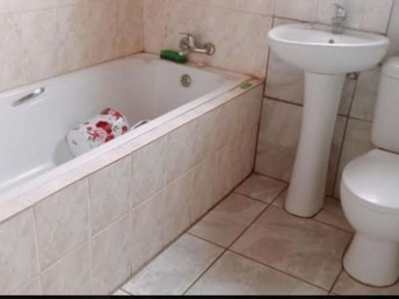 A functional bathroom featuring a standard bathtub, pedestal basin, and toilet with neutral wall and floor tiling.