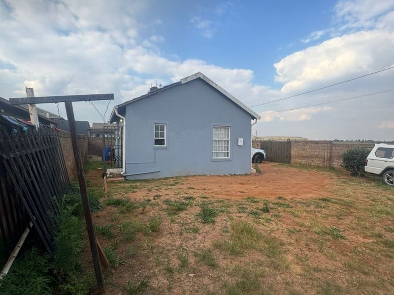 Rear view of the property showing the exterior wall, gabled roof, and a large unpaved backyard area enclosed by perimeter walls.