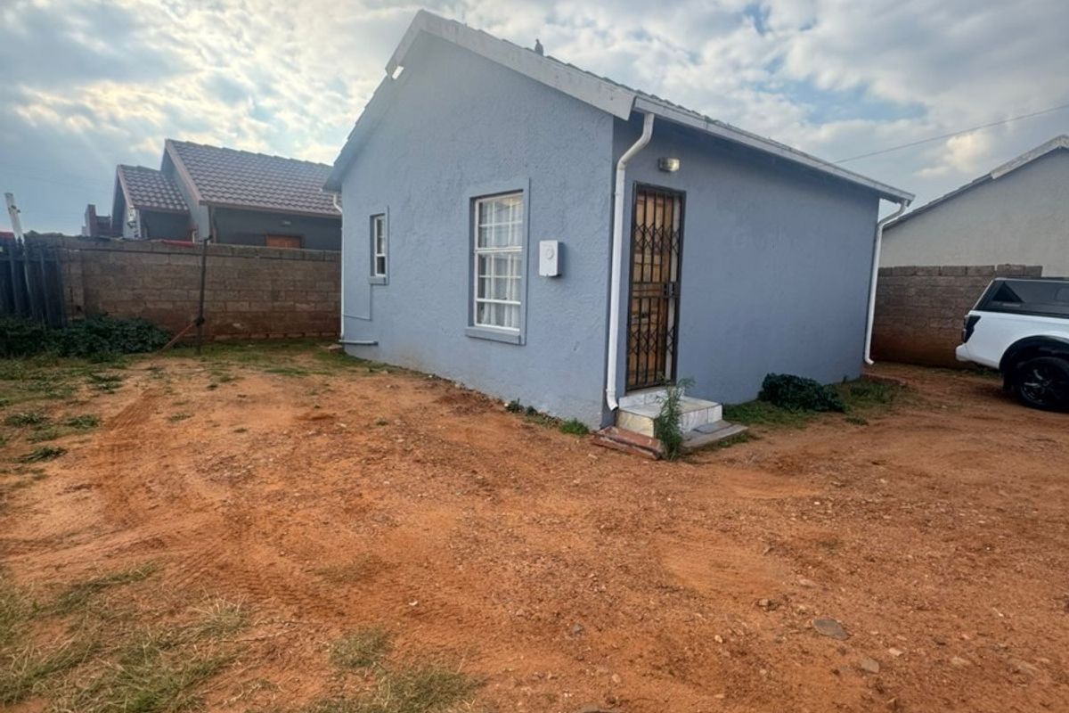 Rear view of a detached house featuring a blue rendered facade, security gate, and an unlandscaped yard with exposed soil.