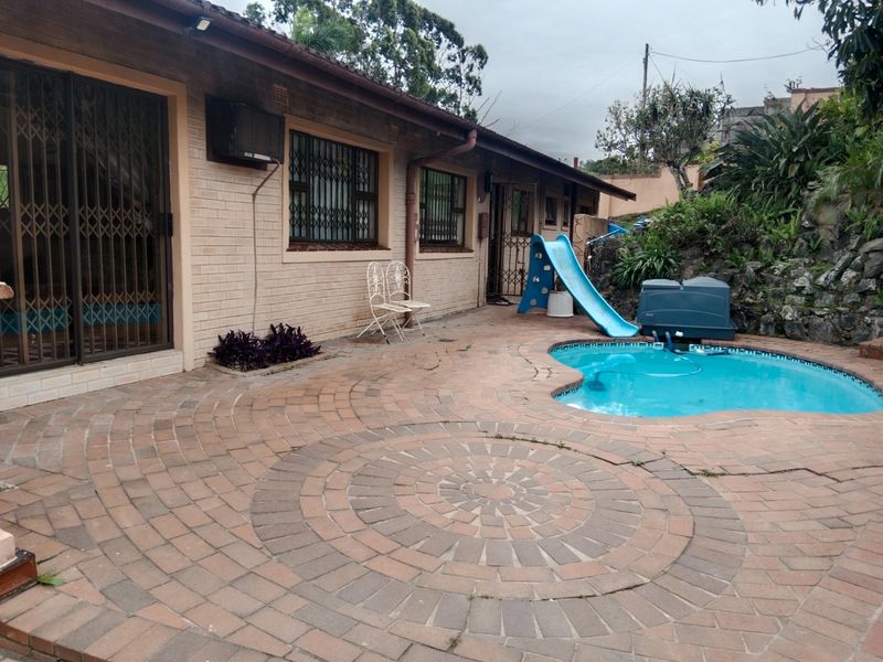 Rear exterior view featuring a brick-paved patio area, a swimming pool, and direct access to the house through sliding doors with security gates.