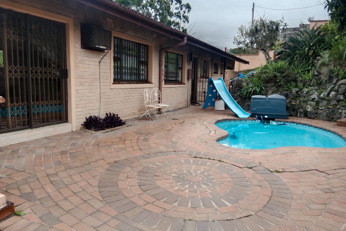 Rear exterior view featuring a brick-paved patio area, a swimming pool, and direct access to the house through sliding doors with security gates.