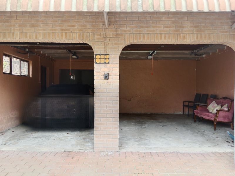 A double garage featuring exposed brickwork, concrete flooring, and integrated garage door motors, showing signs of wear and aging.