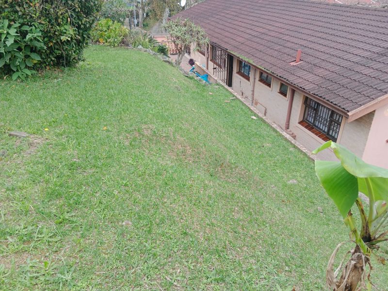 A view of the rear exterior of the house, featuring a sloped lawn area and brick facade with security bars on the windows.