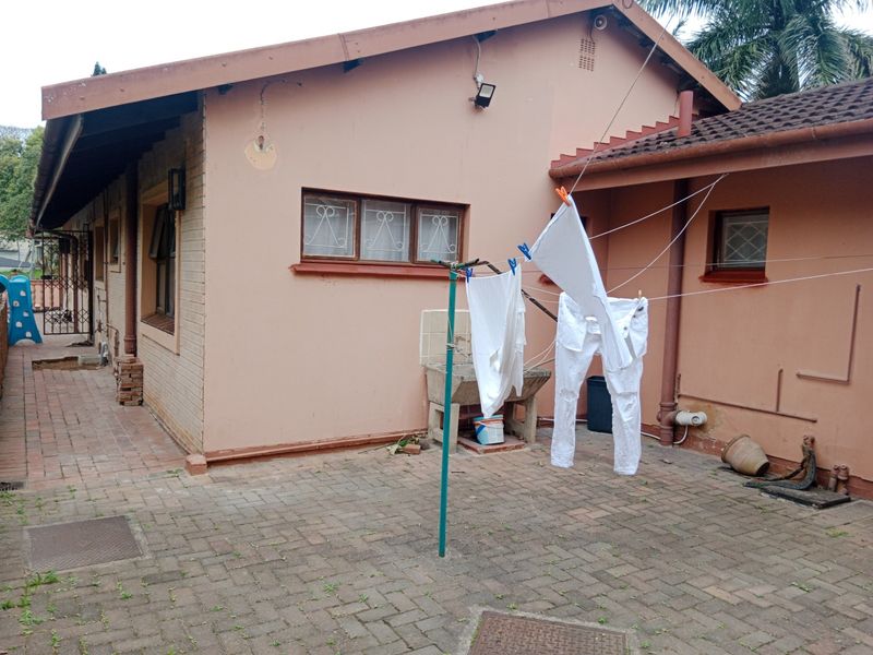 Rear exterior view of the property featuring brick paving, a concrete wash trough, and security bars on the windows.