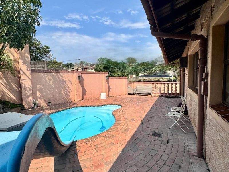 Outdoor pool area featuring a swimming pool with a slide, surrounded by brick paving and a perimeter boundary wall.