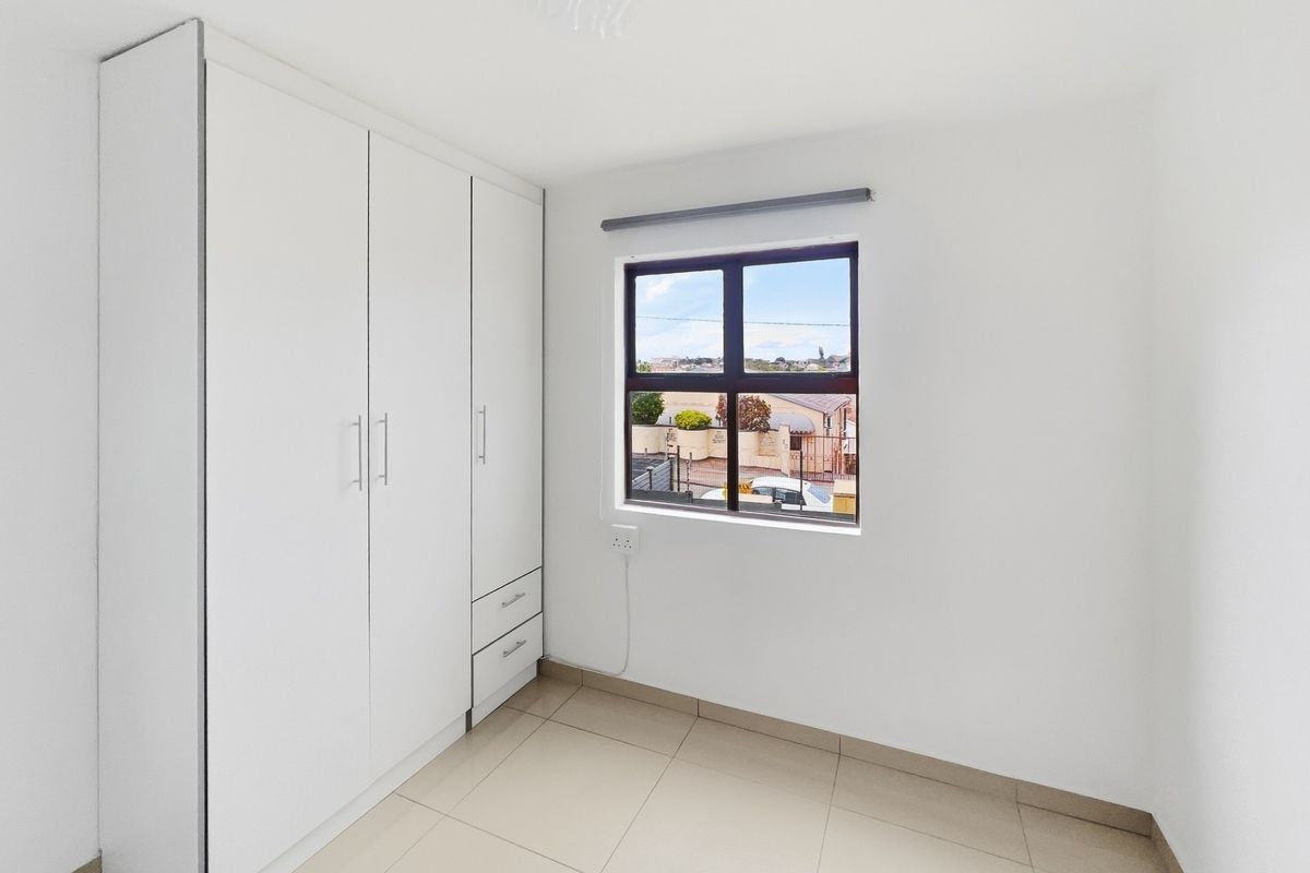 A bright, empty bedroom featuring neutral tiled flooring and modern white built-in cupboards with ample storage space.