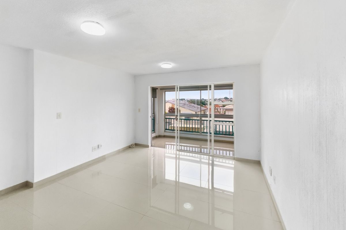 A bright, empty living room featuring polished tile flooring and a large sliding glass door providing access to a private balcony.