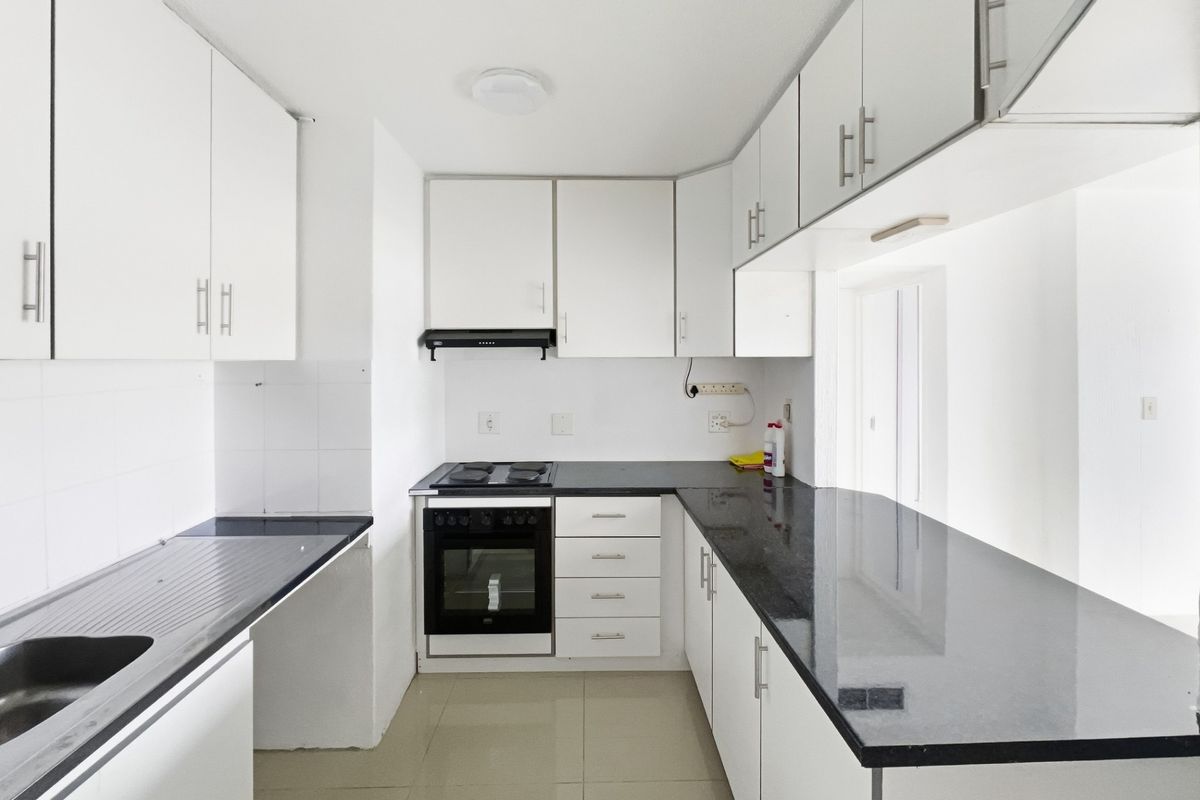 A clean, functional kitchen featuring white cabinetry, dark granite countertops, an integrated oven and stove, and neutral tiled flooring.