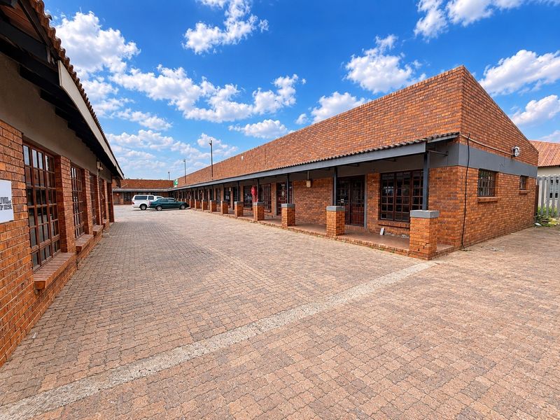 A commercial property featuring a face brick facade, a paved driveway, and a covered walkway with timber-framed windows and doors.
