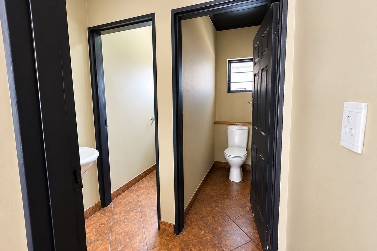 A functional commercial bathroom area featuring tiled flooring, a standard toilet, and a wall-mounted basin with dark-painted door frames.