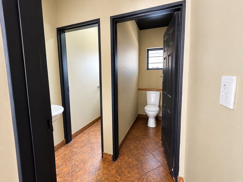A functional commercial bathroom area featuring tiled flooring, a standard toilet, and a wall-mounted basin with dark-painted door frames.