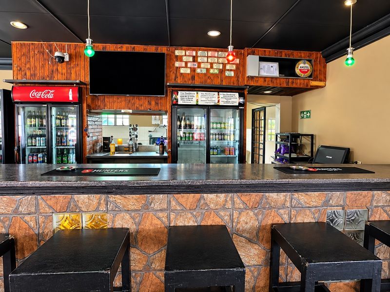 A commercial bar area featuring a stone-clad counter, wood-paneled back bar, integrated commercial refrigeration units, and decorative pendant lighting.