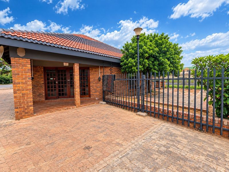 Front exterior view of a commercial property featuring a brick facade, covered entrance porch, paved driveway, and secure metal perimeter fencing.