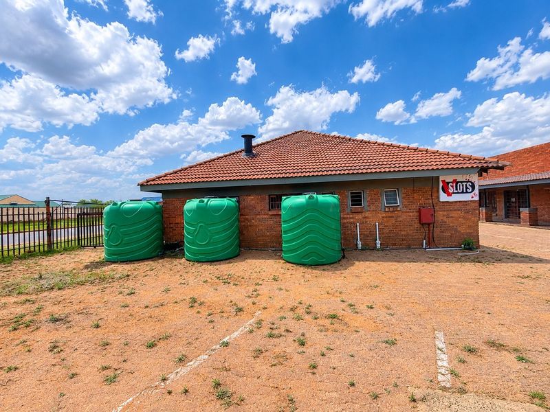 Rear exterior view of a commercial building featuring brick construction, a tiled roof, and three large green water storage tanks.