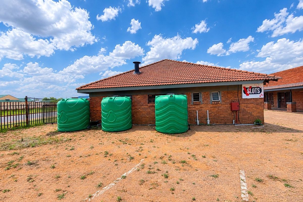 Rear exterior view of a commercial building featuring brick construction, a tiled roof, and three large green water storage tanks.