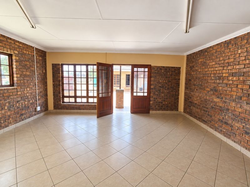 Spacious interior room featuring exposed brick walls, ceramic tiled flooring, and timber-framed glass doors leading to an outdoor area.