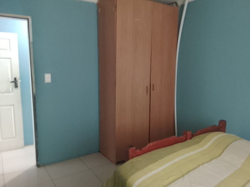 A bedroom featuring tiled flooring, a built-in wardrobe, and blue painted walls with visible surface imperfections and exposed wiring.