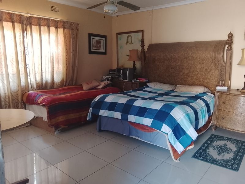 A spacious bedroom featuring tiled flooring, a ceiling fan, and neutral wall finishes, offering a functional layout for sleeping arrangements.