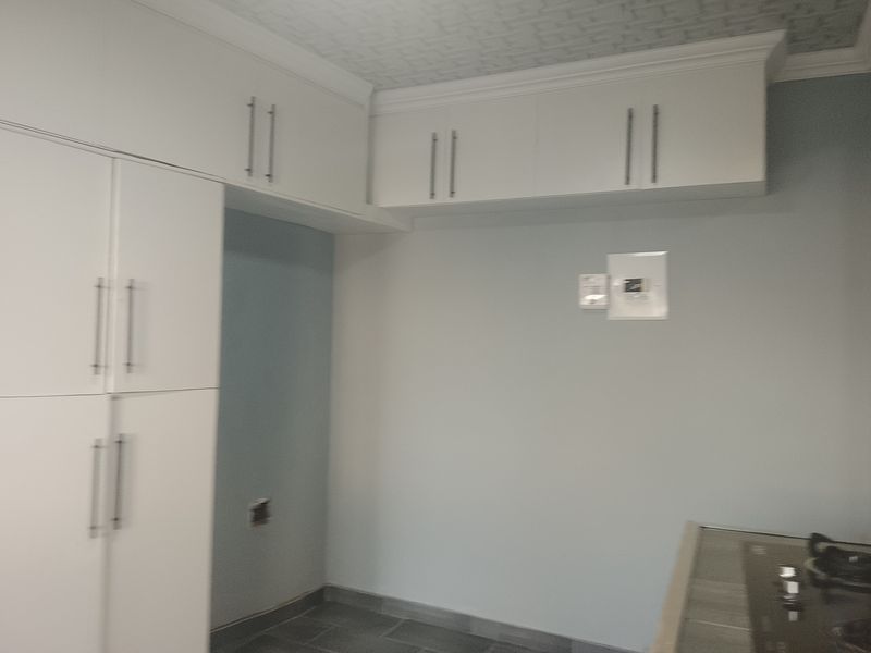 A clean, modern kitchen area featuring white built-in cabinetry, overhead storage, and a fitted hob, presenting a neutral and functional space.