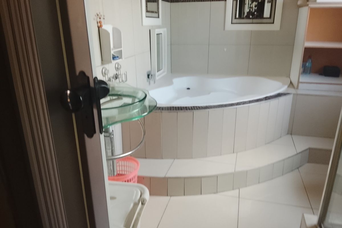 A bathroom featuring a raised corner bathtub with tiled surround, a glass pedestal basin, and neutral wall tiling.