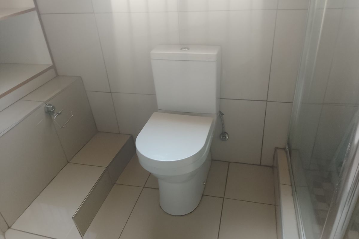 A clean, functional bathroom featuring a modern toilet, tiled finishes, and a glass-enclosed shower area with built-in storage shelving.