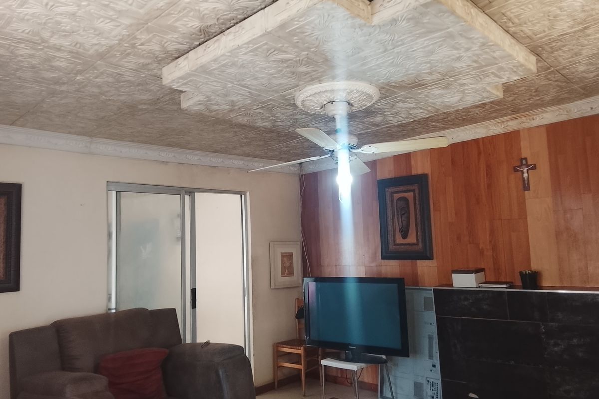 Living room featuring decorative ceiling tiles, a ceiling fan, wood paneling, and a tiled fireplace surround with sliding door access.