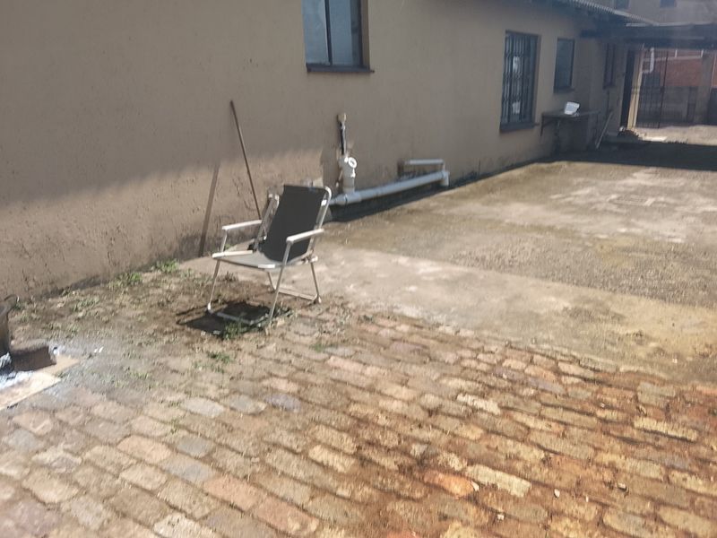 Rear exterior area featuring brick paving, a concrete apron, and external plumbing fixtures along the building wall.