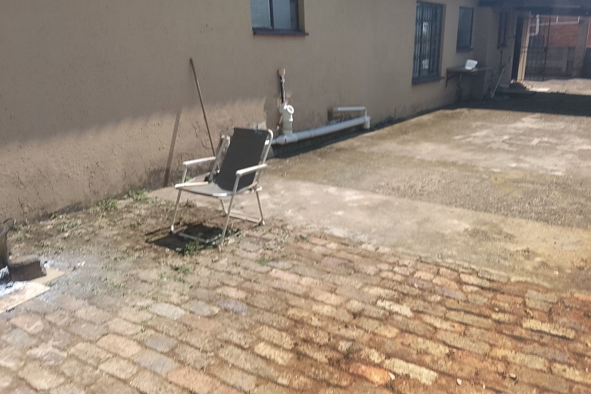Rear exterior area featuring brick paving, a concrete apron, and external plumbing fixtures along the building wall.