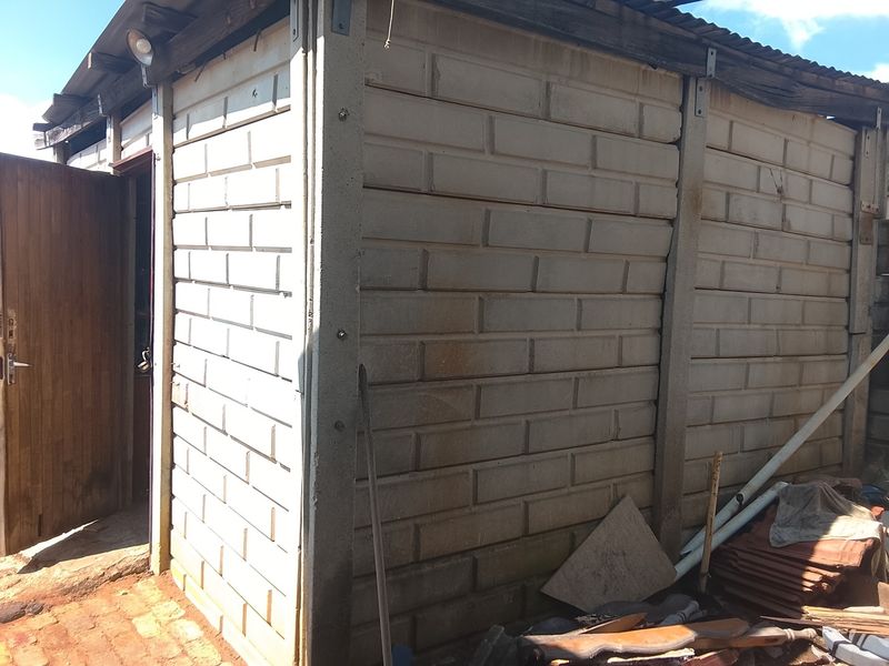 A detached utility structure featuring precast concrete walling and a corrugated metal roof, currently showing signs of significant weathering and wear.