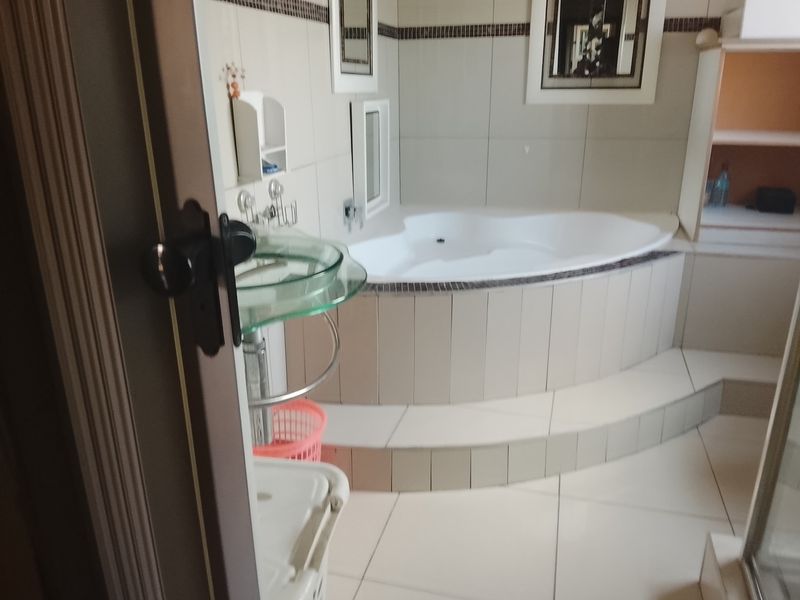 A bathroom featuring a raised corner bathtub with tiled surround, a glass pedestal basin, and neutral wall tiling.