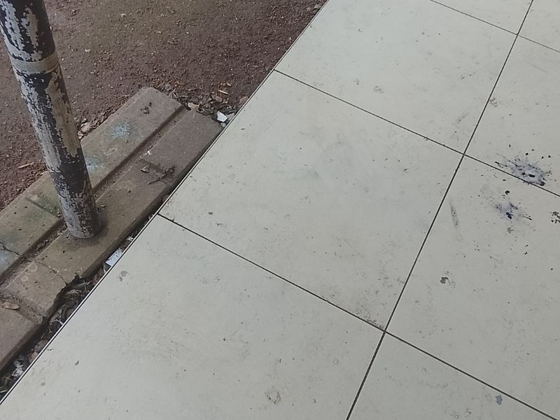A close-up view of a tiled outdoor patio area showing signs of wear, including surface staining and a weathered metal support post.