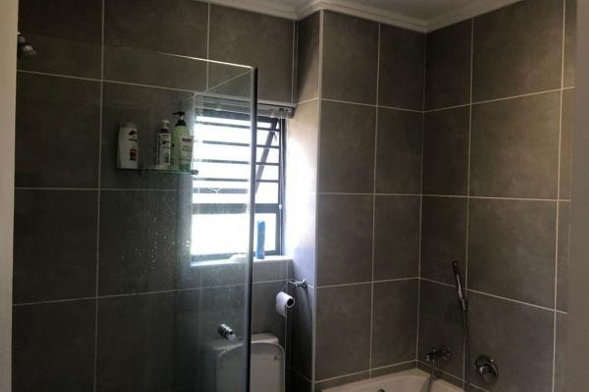 A modern bathroom featuring grey wall tiles, a glass-enclosed shower, and a bathtub with a handheld shower mixer.