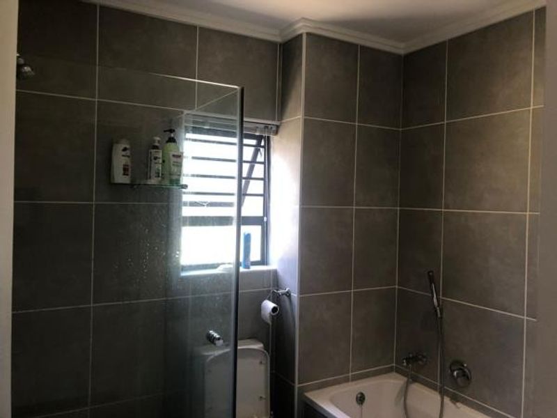 A modern bathroom featuring grey wall tiles, a glass-enclosed shower, and a bathtub with a handheld shower mixer.