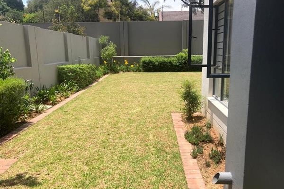 A well-maintained rear garden featuring a manicured lawn, brick-edged garden beds, and a secure perimeter wall.