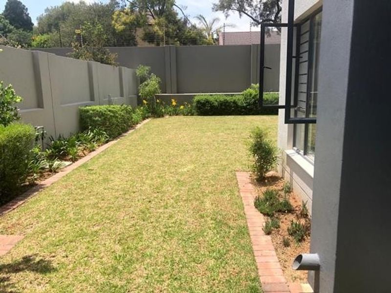 A well-maintained rear garden featuring a manicured lawn, brick-edged garden beds, and a secure perimeter wall.