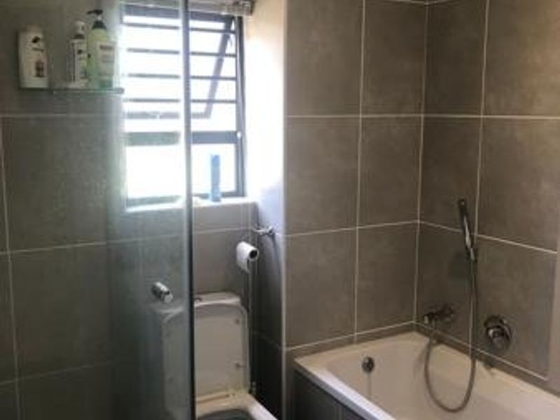 Modern bathroom featuring a glass-enclosed shower, a built-in bathtub with handheld shower head, and neutral grey wall tiling.