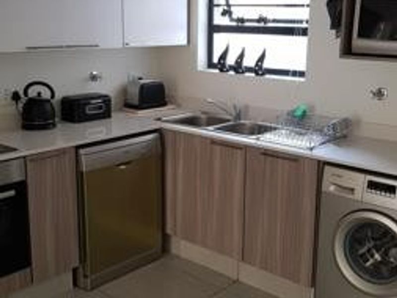 A functional kitchen featuring light wood-tone lower cabinetry, white upper cabinets, tiled flooring, and integrated appliances including a dishwasher and washing machine.