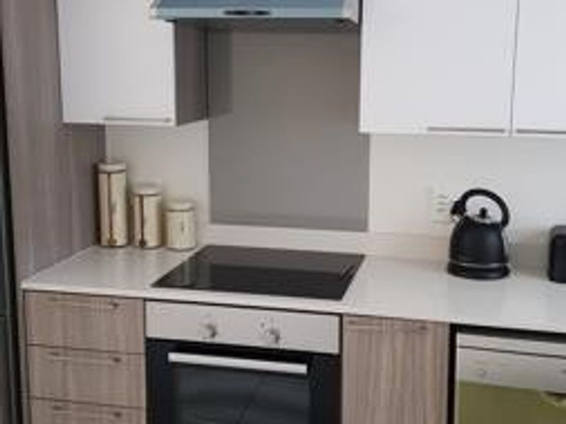 Modern kitchen featuring white and wood-grain cabinetry, stone countertops, a built-in oven, electric cooktop, and extractor fan with tiled flooring.