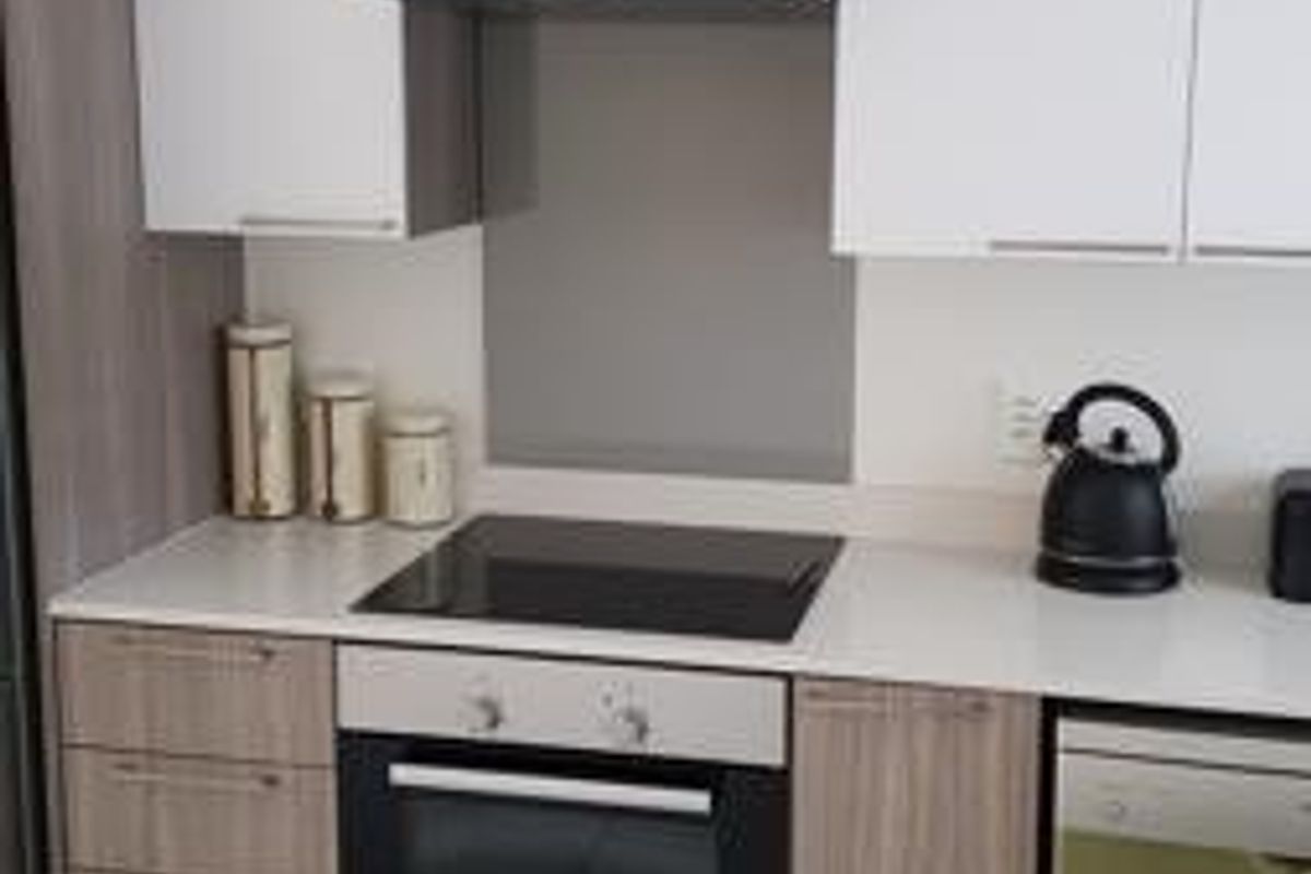 Modern kitchen featuring white and wood-grain cabinetry, stone countertops, a built-in oven, electric cooktop, and extractor fan with tiled flooring.
