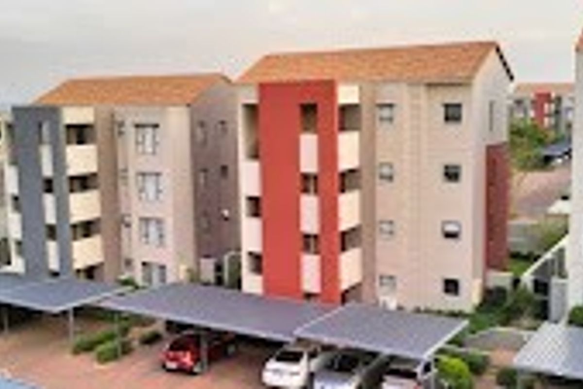 Aerial view of a modern apartment complex featuring multi-story residential buildings with tiled roofs and dedicated covered carport parking areas.