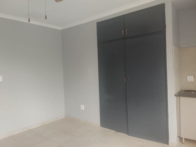 A clean, empty bedroom featuring neutral grey walls, tiled flooring, and dark built-in cupboards with overhead storage.
